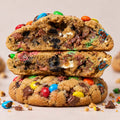 Stacked chocolate chip cookies filled with colorful M&M's and OREO, shown close-up on a light beige background.