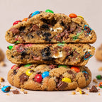 Stacked chocolate chip cookies filled with colorful M&M's and OREO, shown close-up on a light beige background.