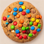 A large chocolate chip cookie topped with colorful candy-coated chocolate pieces, photographed from directly above on a plain light beige background.